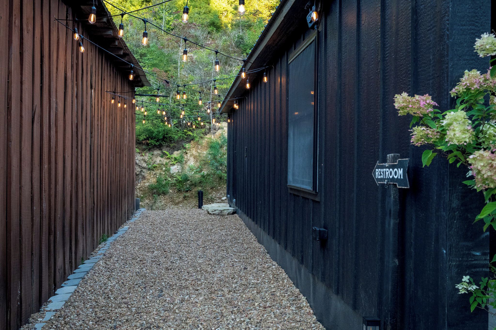 A narrow pathway flanked by wooden buildings with a sign indicating a restroom.