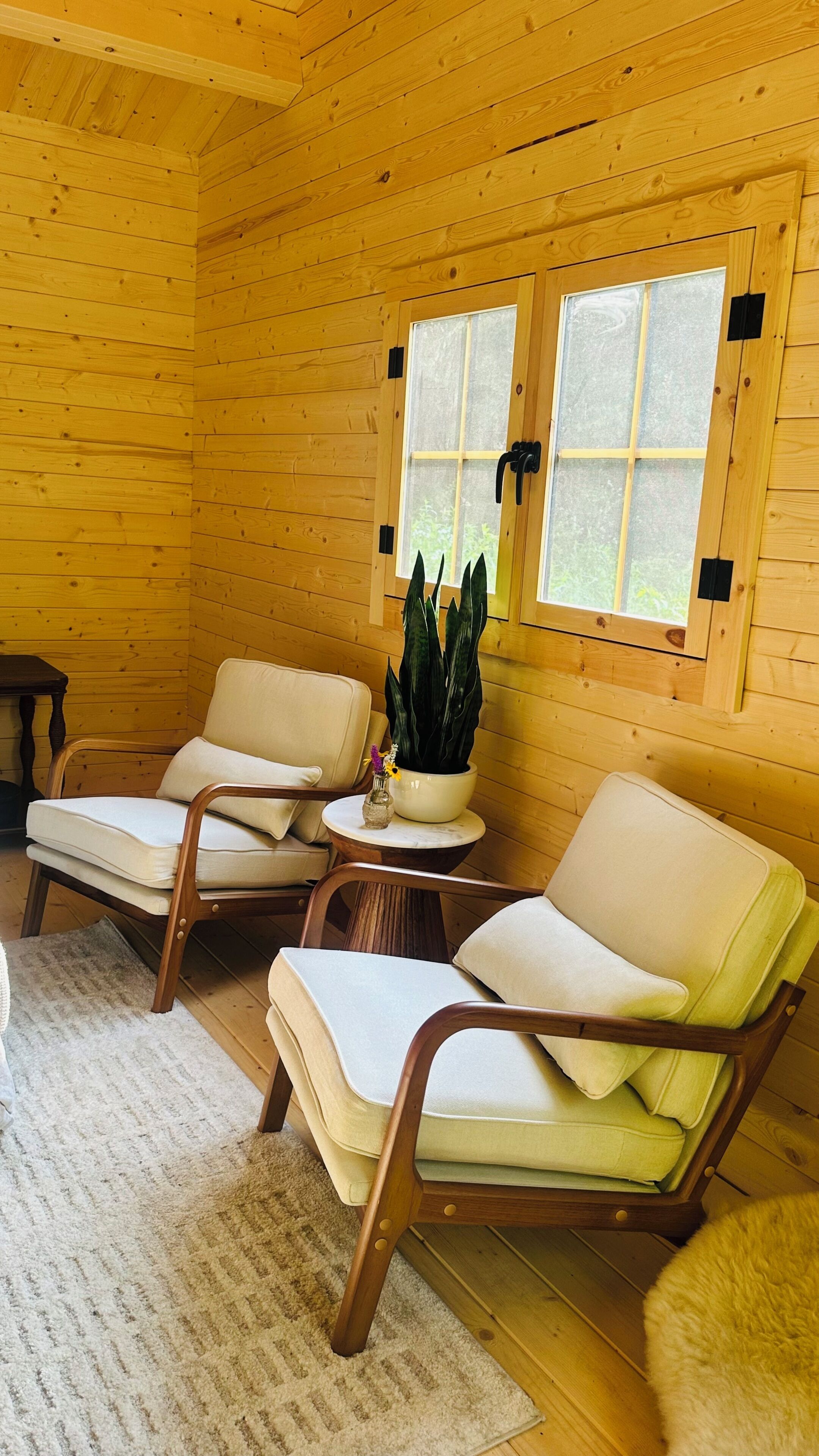 A cozy cabin interior with two wooden chairs, a small table with a plant, and a window with a view.