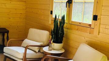 A cozy cabin interior with two wooden chairs, a small table with a plant, and a window with a view.