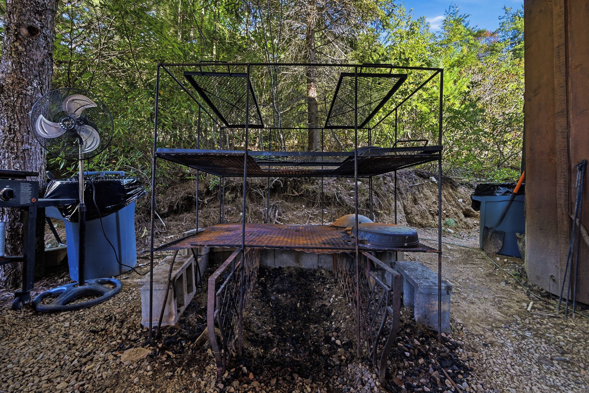 Una estructura metálica con techo, rodeada de árboles y grava.