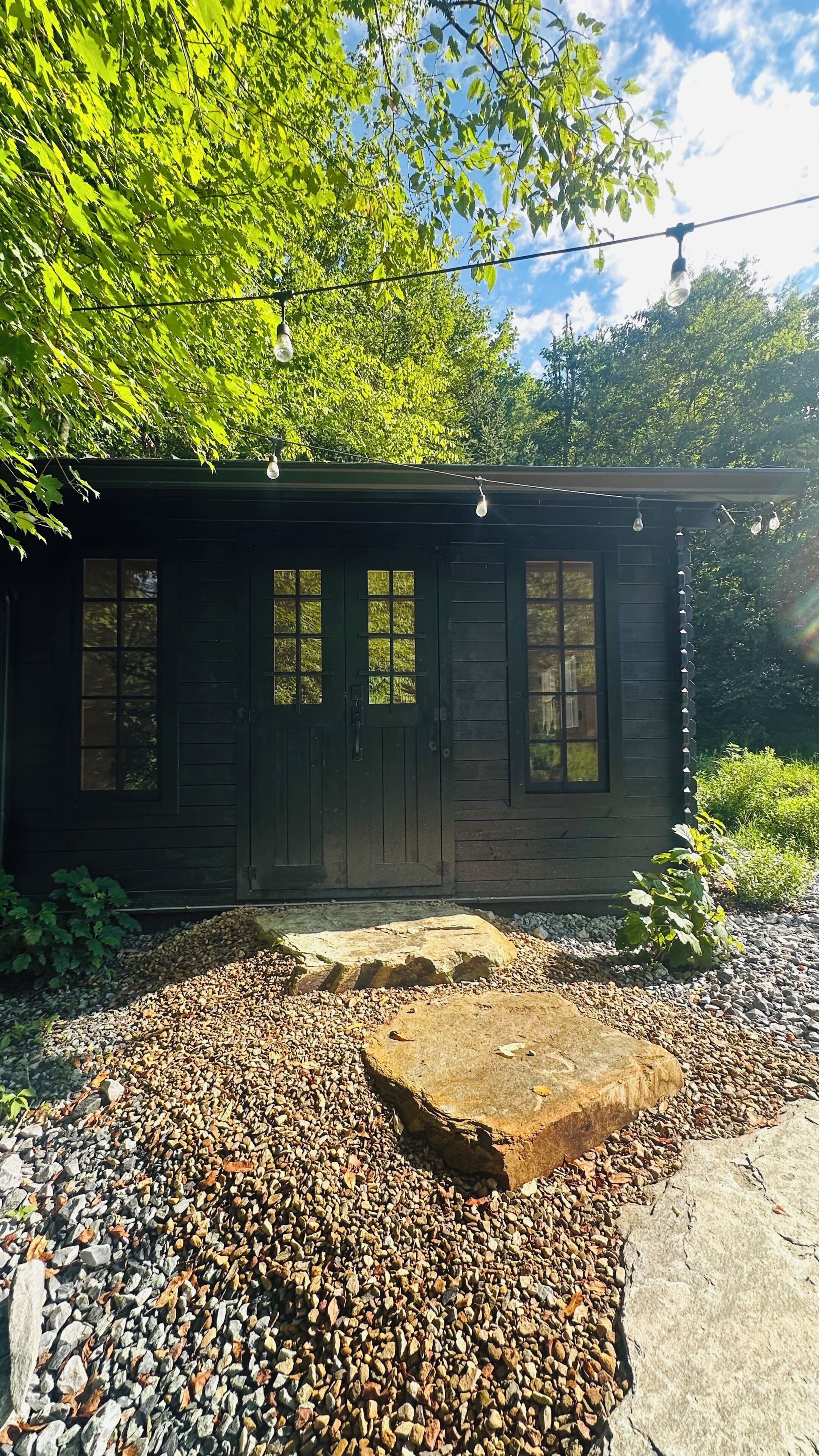 A wooden cabin with a gravel driveway, surrounded by trees.