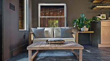 A modern living room with a wooden coffee table, a sofa with patterned cushions, a potted plant, and a window with curtains.
