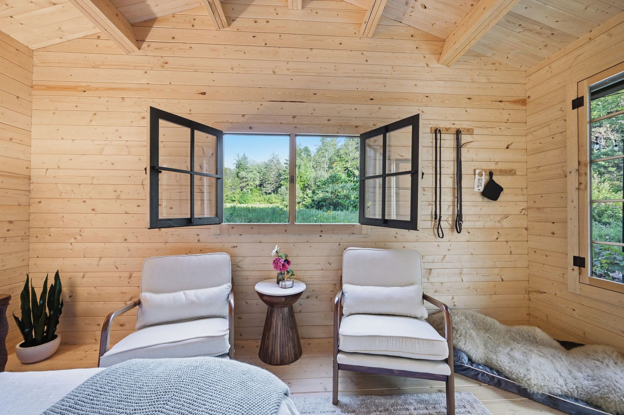 Interior acogedor de una cabaña con dos sillones, una mesita con un florero, y un ventanal con vistas a la vegetación.