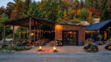 A rustic cabin with a covered outdoor seating area, a fire pit, and a garden with colorful flowers.