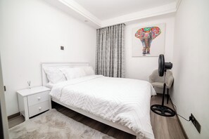Ein modernes Schlafzimmer mit einem Bett, einem Nachttisch und einem Standventilator.