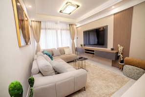 A modern living room with a sectional sofa, a flat-screen TV, and a minimalist design. - Charming 2BR apartment in beautiful Nairobi I Private Balcony & City Views (Nairobi)