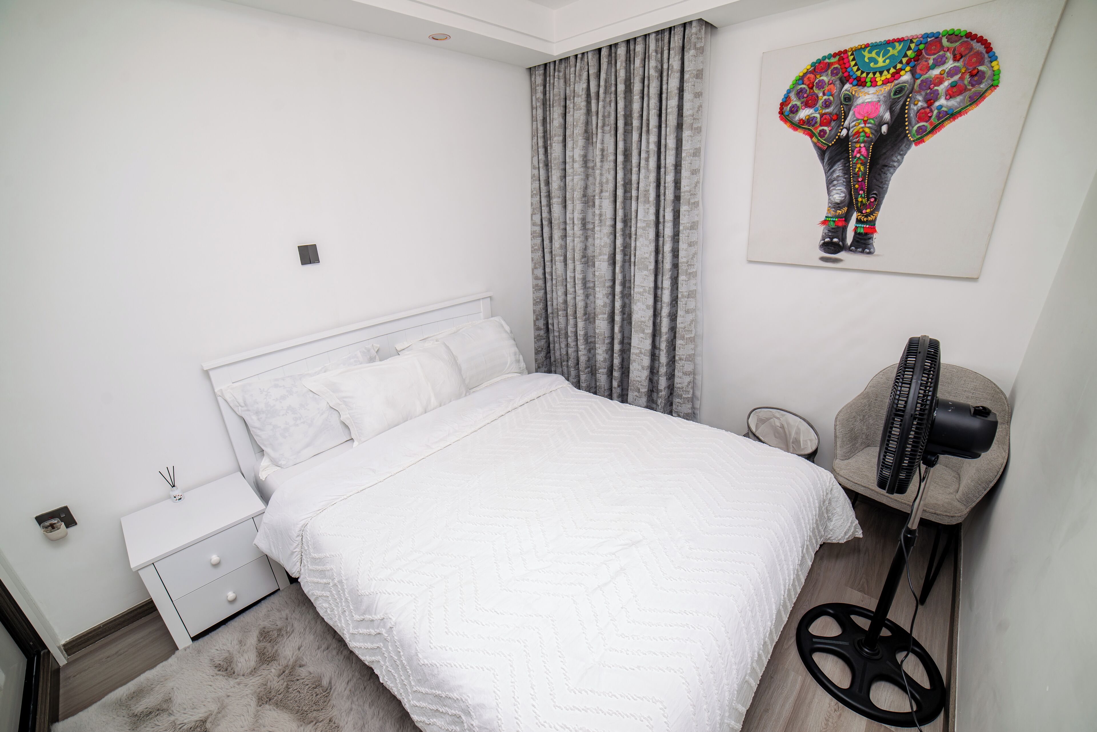 A bedroom with a bed, a nightstand, a lamp, and a wall-mounted picture.