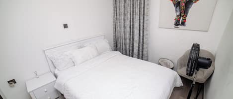 A bedroom with a bed, a nightstand, a lamp, and a wall-mounted picture.