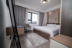 A modern hotel room with a bed, a desk, a chair, and a large window with a city view. - Charming 2BR apartment in beautiful Nairobi I Private Balcony & City Views (Nairobi)