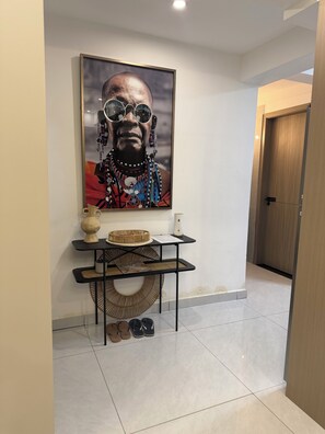A hallway with a framed artwork, a small table with decorative items, and a pair of shoes. - Charming 2BR apartment in beautiful Nairobi I Private Balcony & City Views (Nairobi)