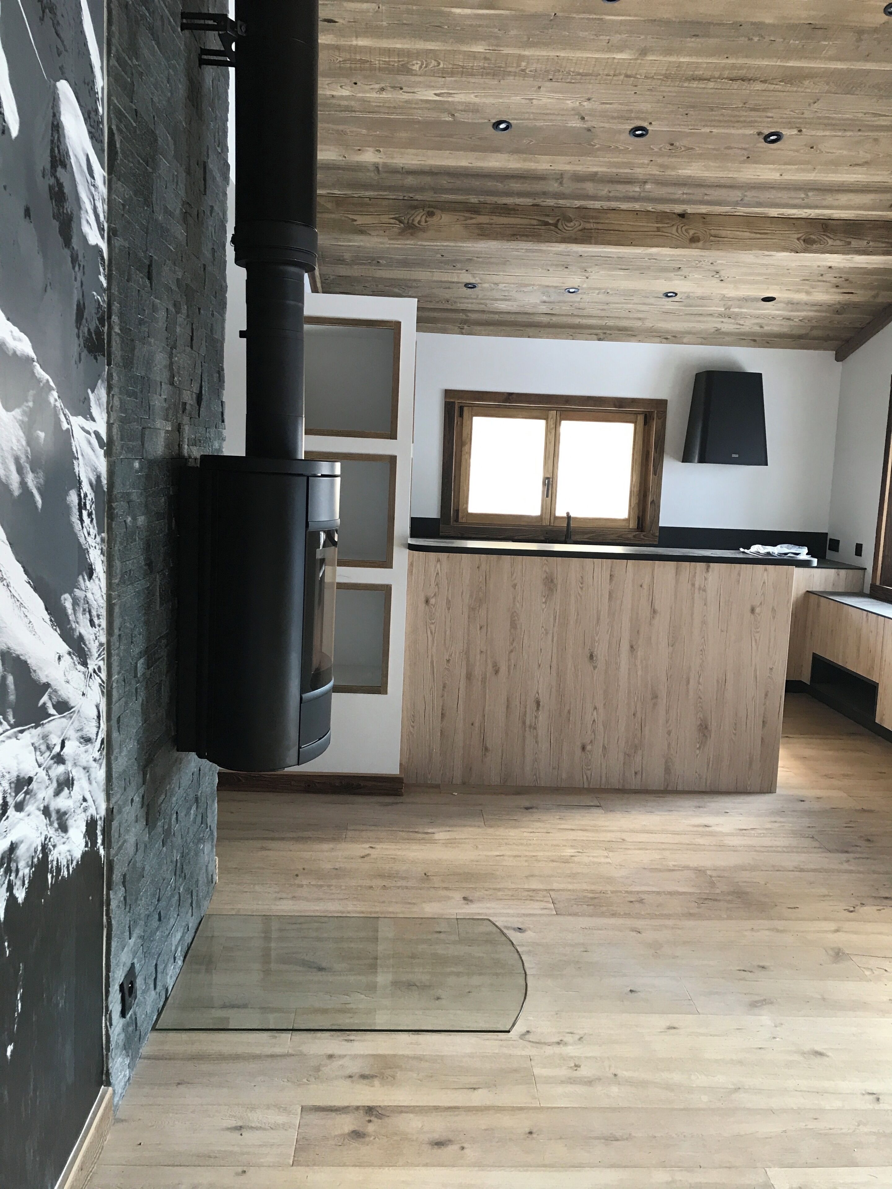 A modern kitchen with a central island, wooden ceiling, and a large window.