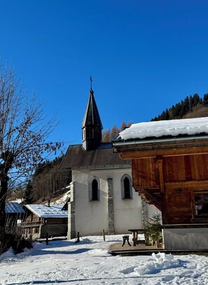 A church with a steeple, surrounded by snow-covered ground and buildings. - 2-bedroom beautiful apartment in charming Alpes village close to Mont Blanc. (La Giettaz)