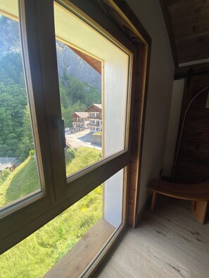 A room with a large window overlooking a mountainous area and a building. - 2-bedroom beautiful apartment in charming Alpes village close to Mont Blanc. (La Giettaz)