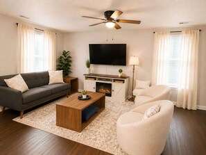 Ein Wohnzimmer mit Sofa, Sessel, Couchtisch, Fernseher, Kamin und Deckenventilator.