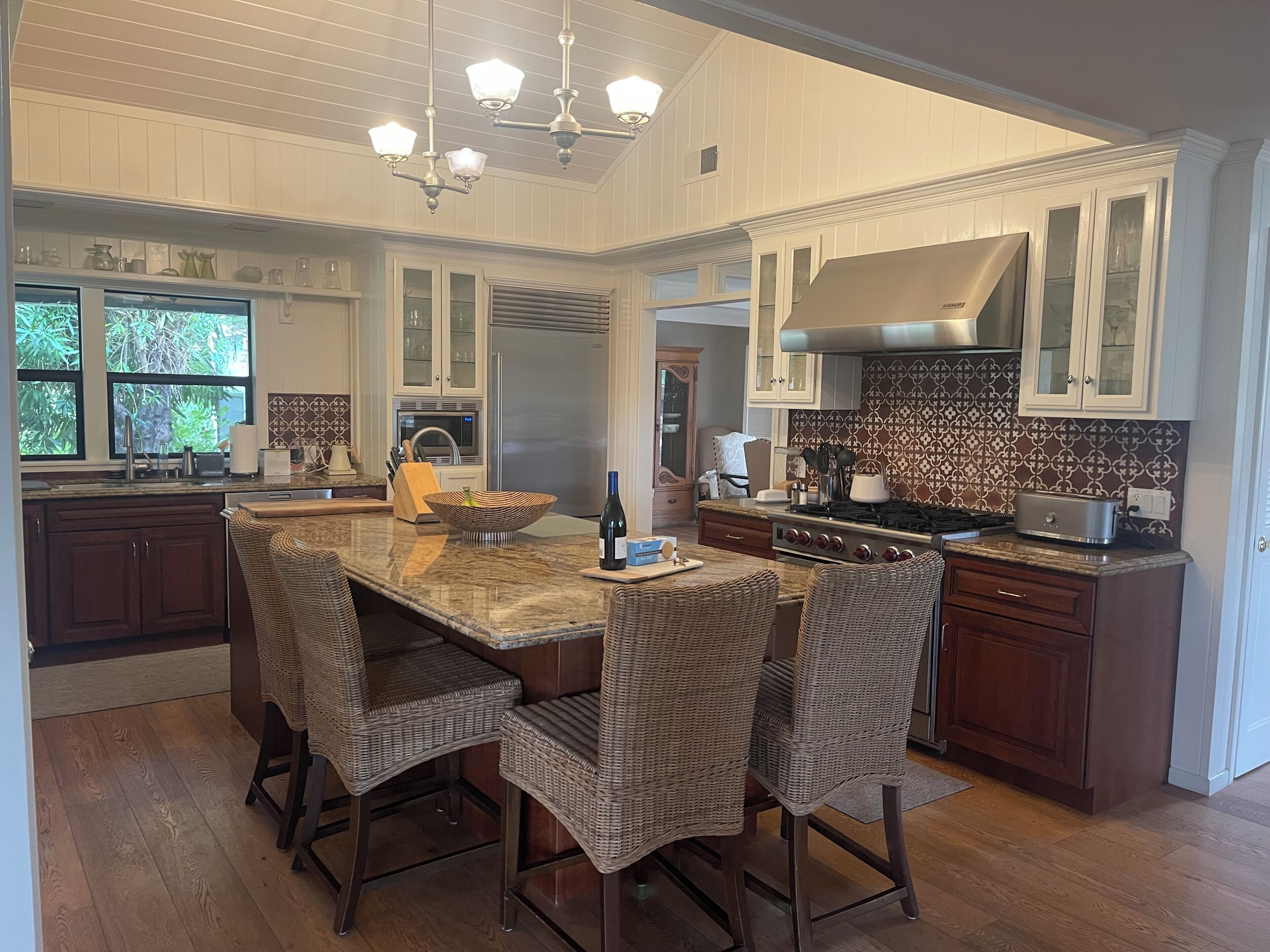 A kitchen with a central island, dark wooden cabinets, a stainless steel refrigerator, and a patterned backsplash.