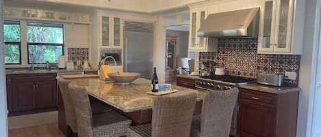 A kitchen with a central island, dark wooden cabinets, a stainless steel refrigerator, and a patterned backsplash.