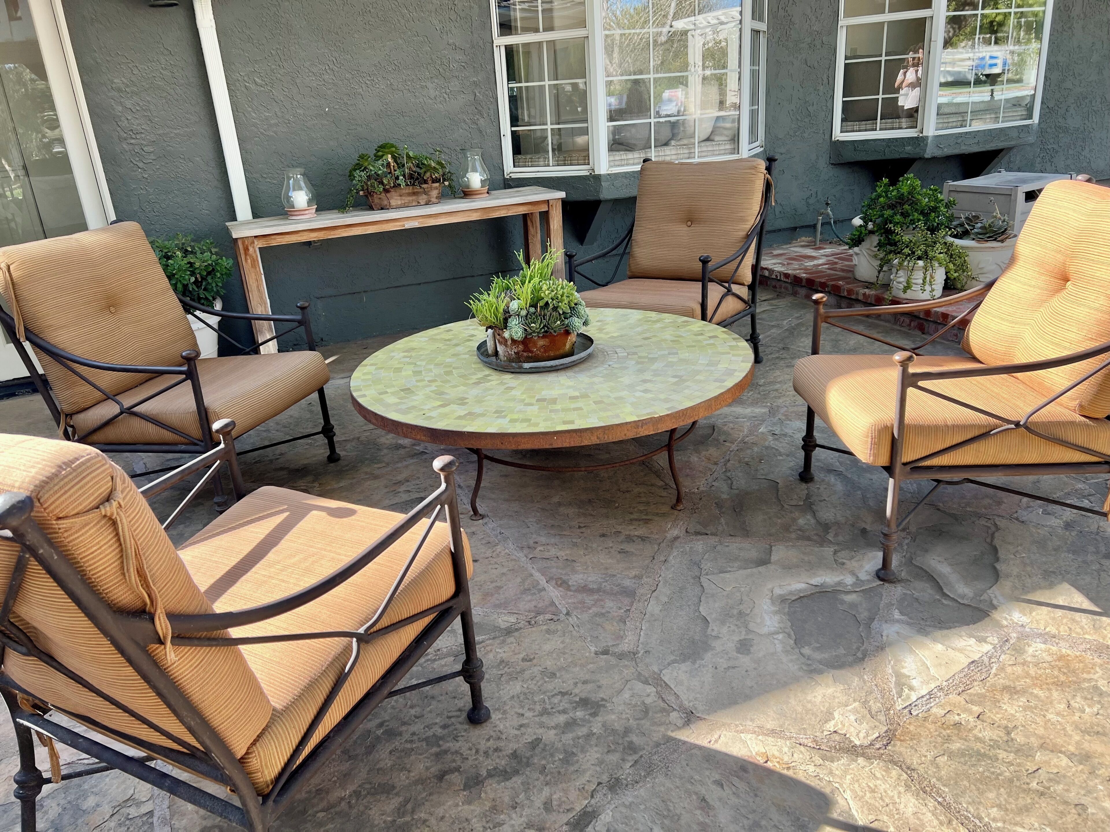 A patio area with a round table surrounded by wicker chairs, potted plants, and a window with a view.