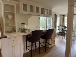 A kitchen with white cabinetry, a glass-top island with two stools, and a view of the outdoors through large windows. - Romance + Luxury at Olive Branch Farm for two in The Santa Ynez Valley. (Solvang)