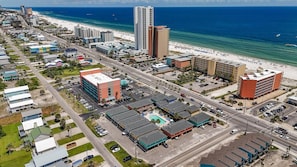 Une vue aérienne d’une ville côtière, avec une plage, des immeubles de grande hauteur et un parking doté d’une piscine.