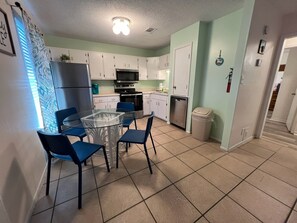 Une cuisine compacte avec des meubles blancs, une table à plateau en verre et des chaises bleues.