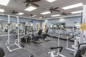 Ein Fitnessraum mit Deckenventilatoren, Trainingsgeräten und einem Fernseher.