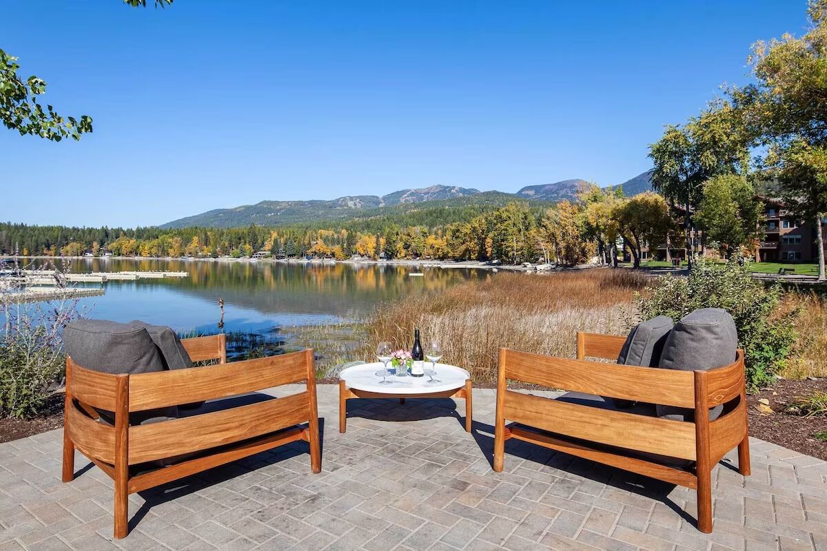 Un conjunto de banco y mesa de madera junto a un lago, con montañas al fondo.