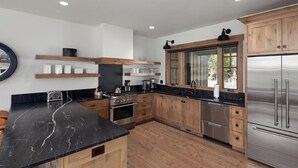 Eine moderne Küche mit Holzschränken, einer schwarzen Marmorarbeitsplatte, Edelstahlgeräten und eingebauten Regalen.