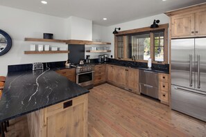 Una cocina moderna con armarios de madera, encimera de mármol negro, electrodomésticos de acero inoxidable y estanterías empotradas.