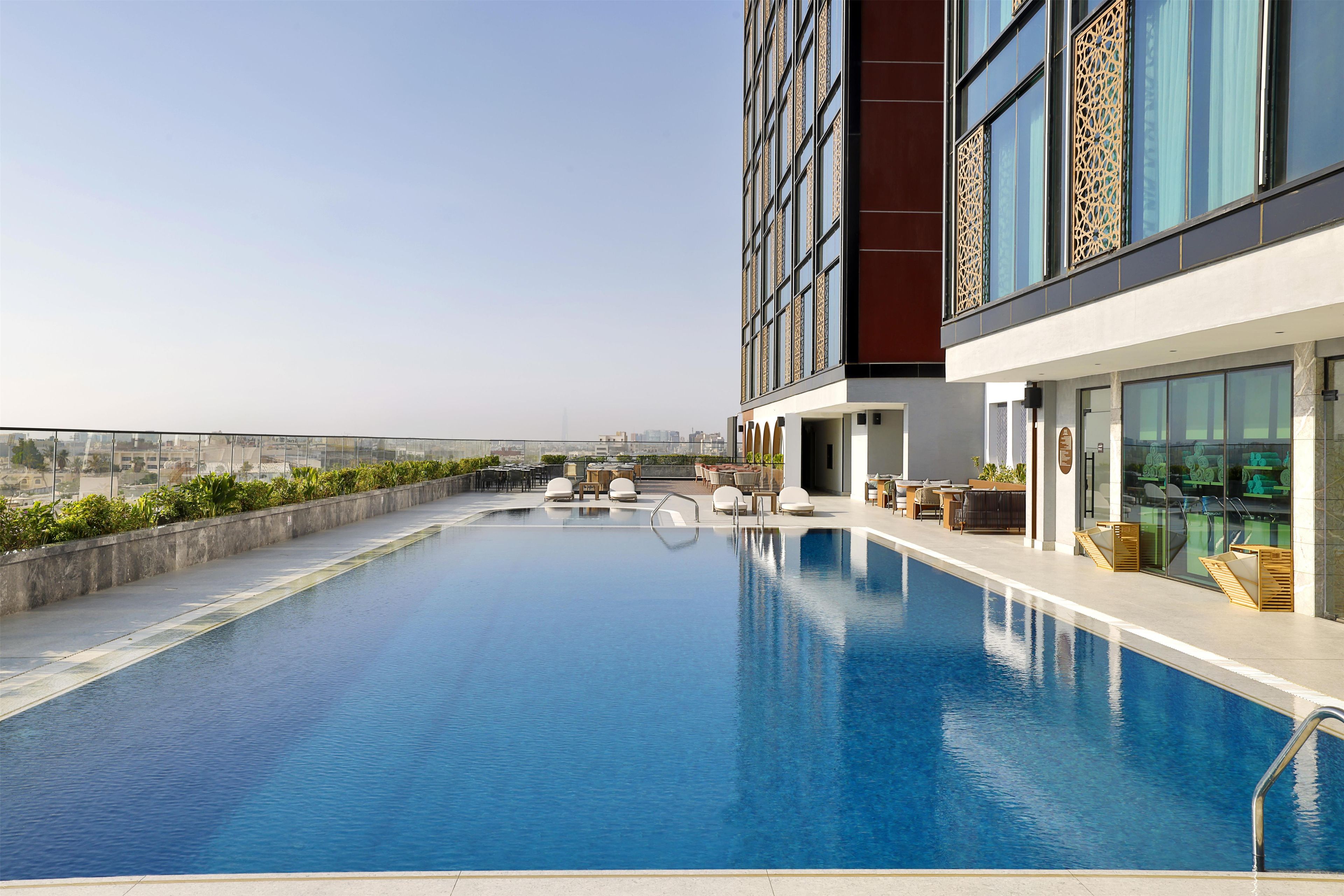 A rooftop swimming pool with a clear view of the city skyline, surrounded by modern buildings and outdoor seating.