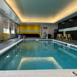 Une piscine intérieure à l’eau claire, avec des chaises jaunes et un poste de surveillance pour le sauveteur.