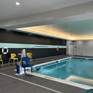 An indoor swimming pool with a lifeguard chair, yellow chairs, and a pool ladder.