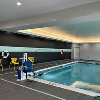 Una piscina interior con una silla de salvavidas, sillas amarillas y una escalera de piscina.