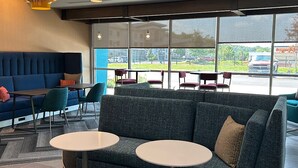 A modern seating area with a sofa and two round tables, large windows with a view of the outside, and pendant lighting. - Tru By Hilton Shippensburg (Shippensburg)