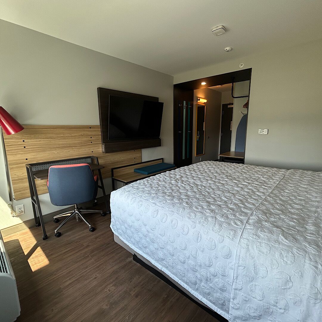 A hotel room with a bed, a desk, a chair, a television, and a mirror.