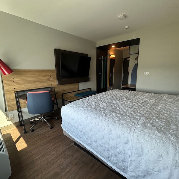 Une chambre d’hôtel équipée d’un lit, d’un bureau, d’une chaise, d’une télévision et d’un miroir.