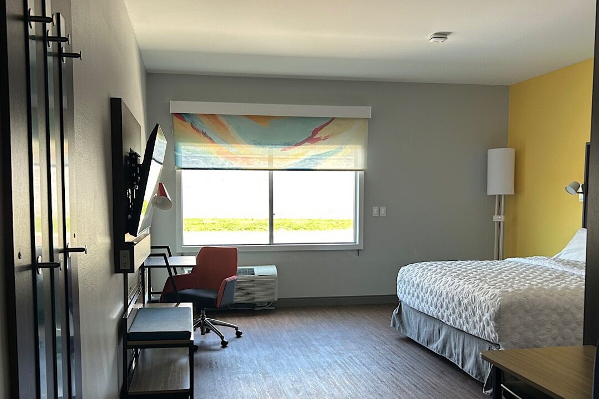A hotel room with a bed, desk, chair, and a large window.