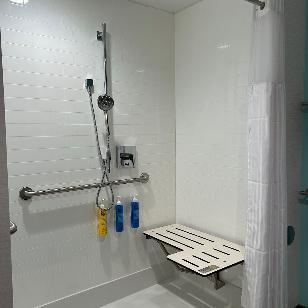 A bathroom with a shower, a hand dryer, and a grab bar.