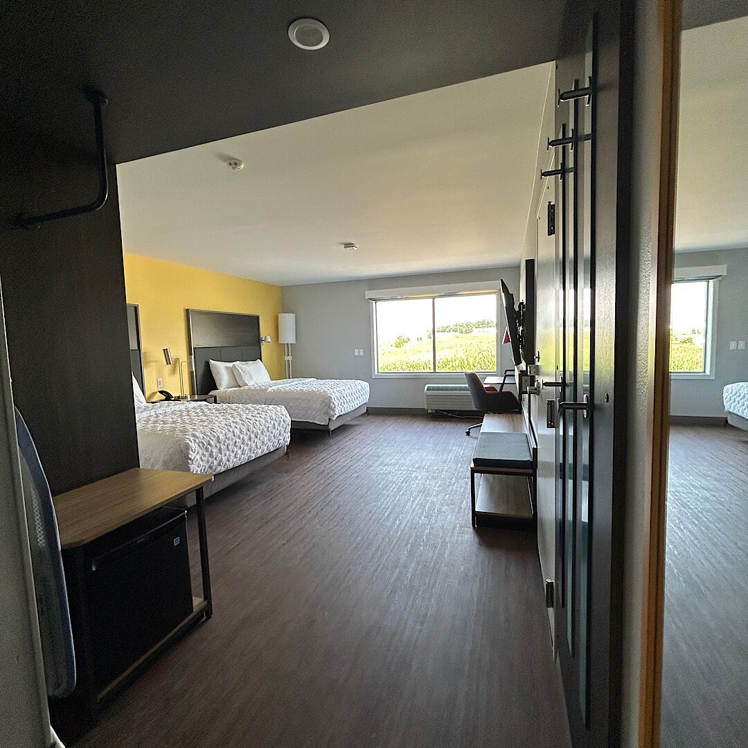 A hotel room with two beds, a desk, and a large window.