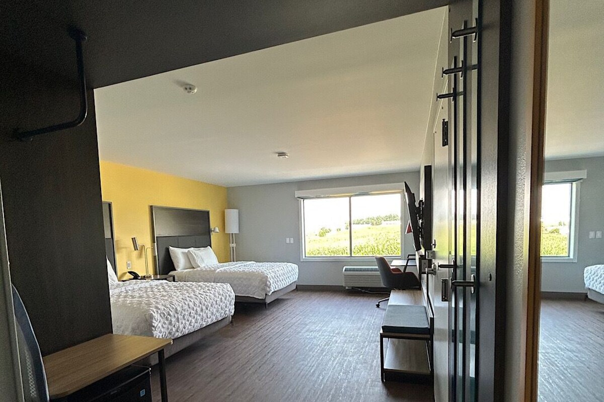 A hotel room with two beds, a desk, and a large window.