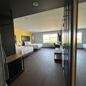 A hotel room with two beds, a desk, and a large window.