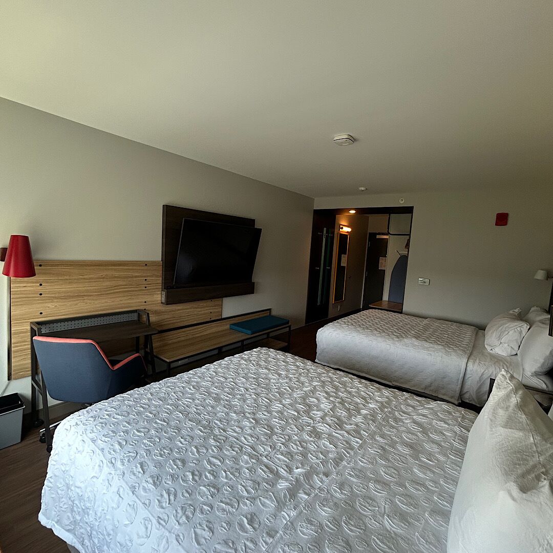 A hotel room with two beds, a desk with a chair, a television, and a mirror.