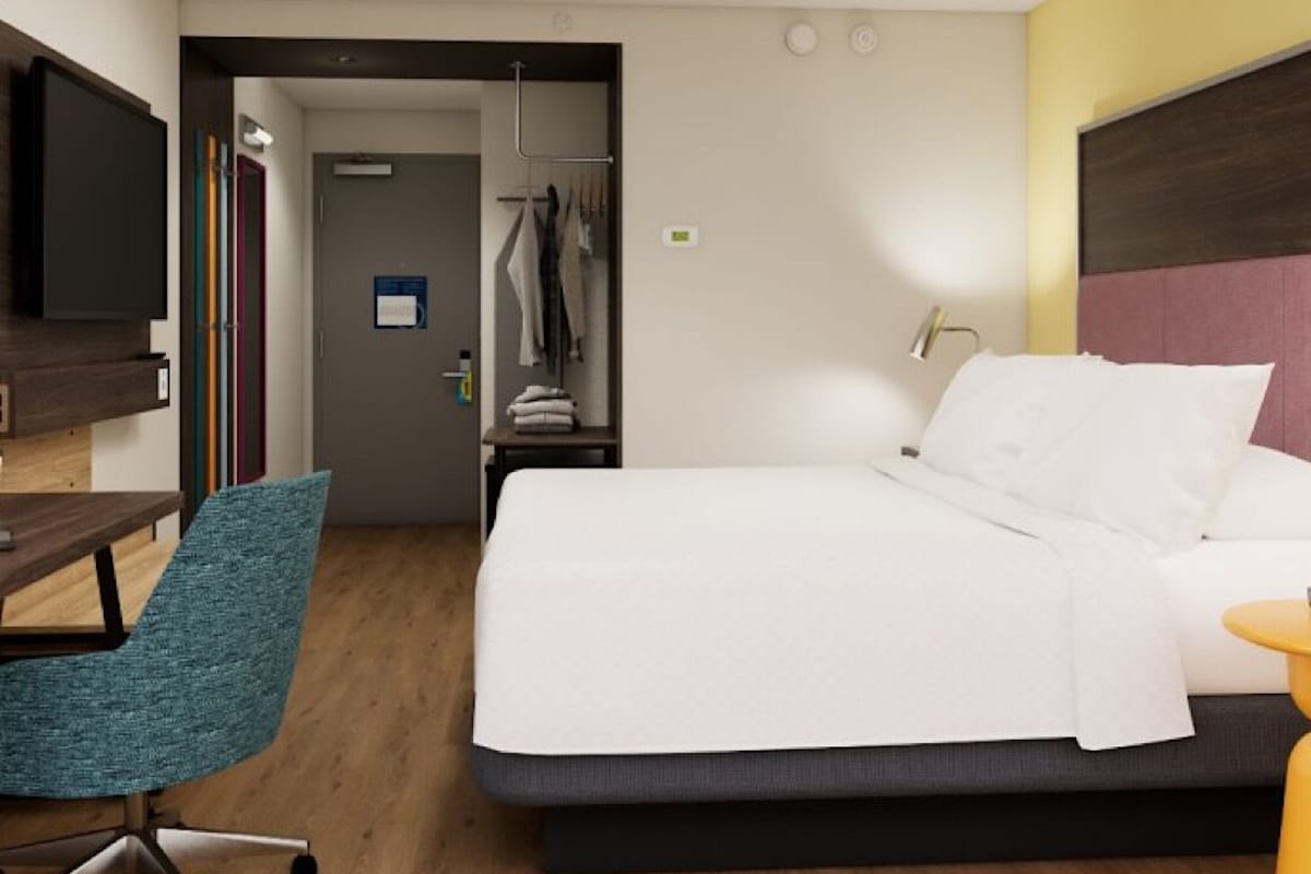 A hotel room with a bed, a desk with a chair, a television, and a wardrobe.