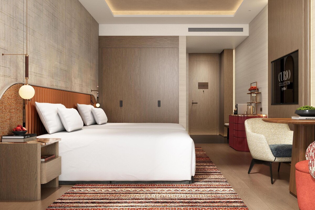 A modern hotel room with a large bed, a desk, a chair, and a television.