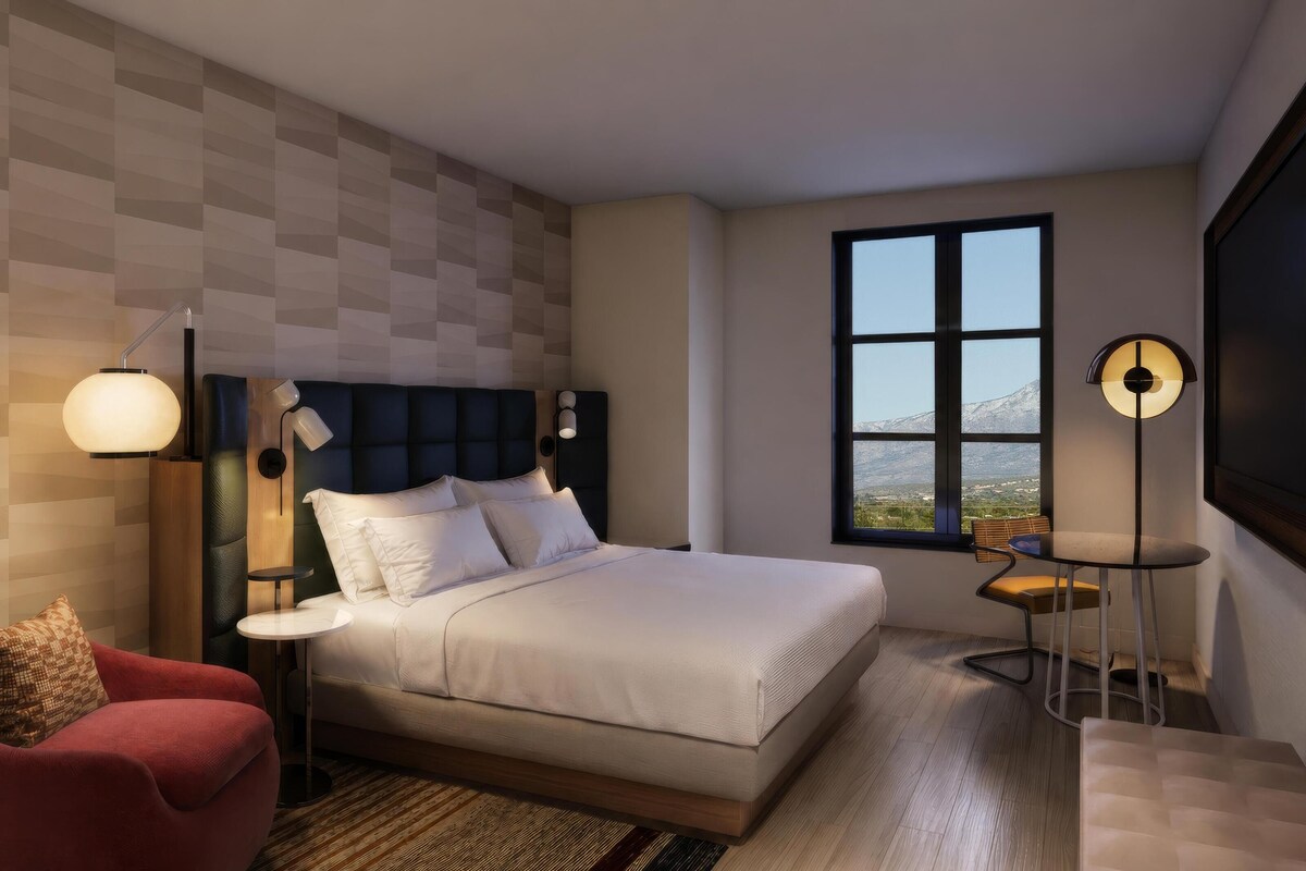Een moderne slaapkamer met een groot bed, een rode fauteuil, een bureau en uitzicht op een berg door een raam.