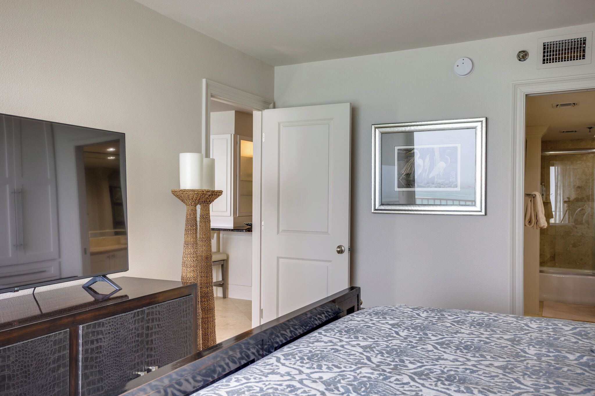 A hotel room with a bed, a TV, a door, and a framed picture on the wall.