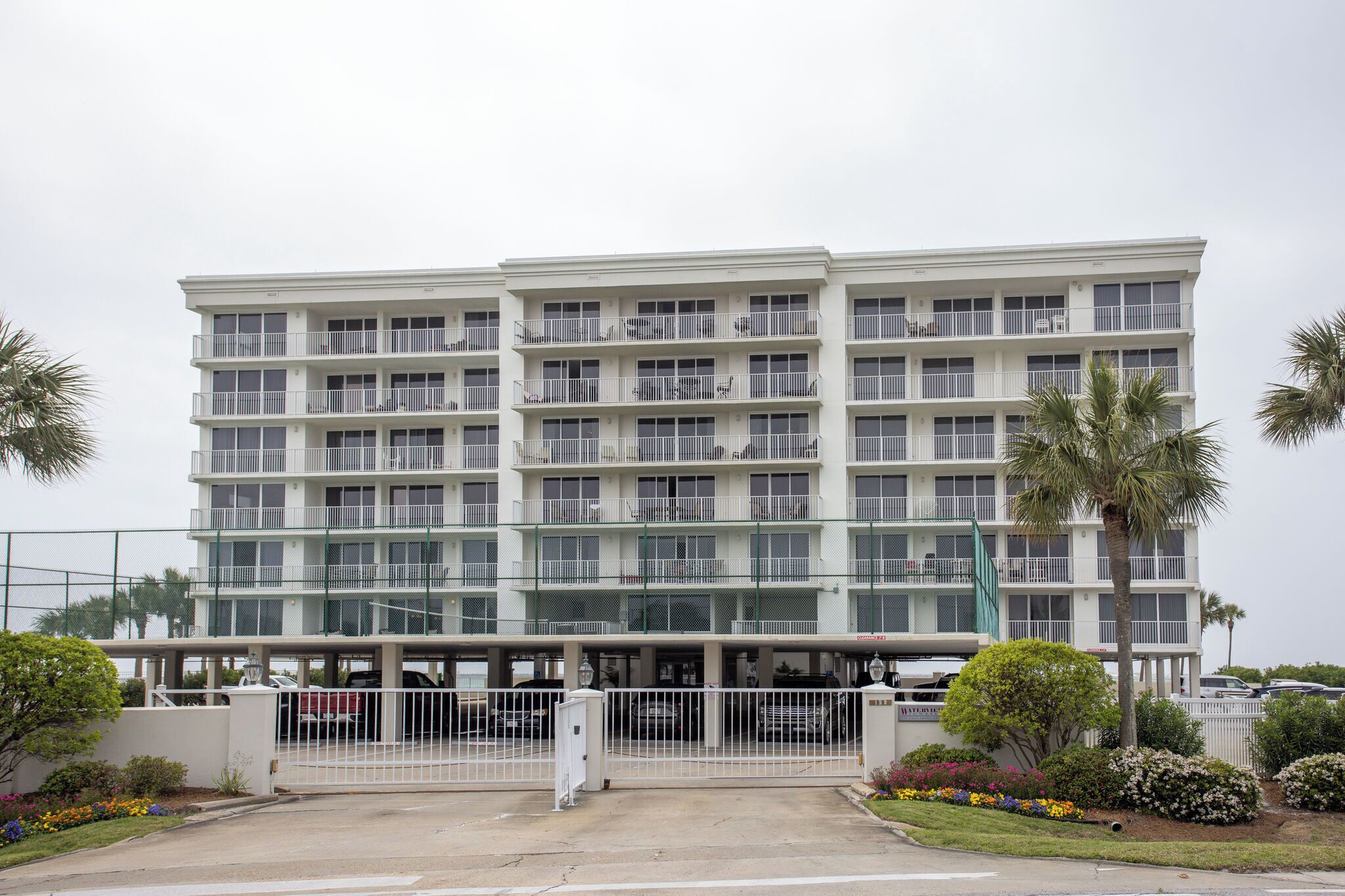 A multi-story hotel with a parking garage, surrounded by greenery and palm trees.