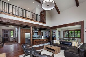 Ein großzügiger Wohnbereich mit hoher Decke, Holzbalken, einem großen Sofa und einer Küche mit Bar.