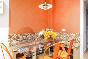 A dining area with a glass table, orange chairs, a patterned sofa, and a vase of flowers. - Vive y trabaja wifi rápido Barcelona Sagrada Metro (Barcelona)