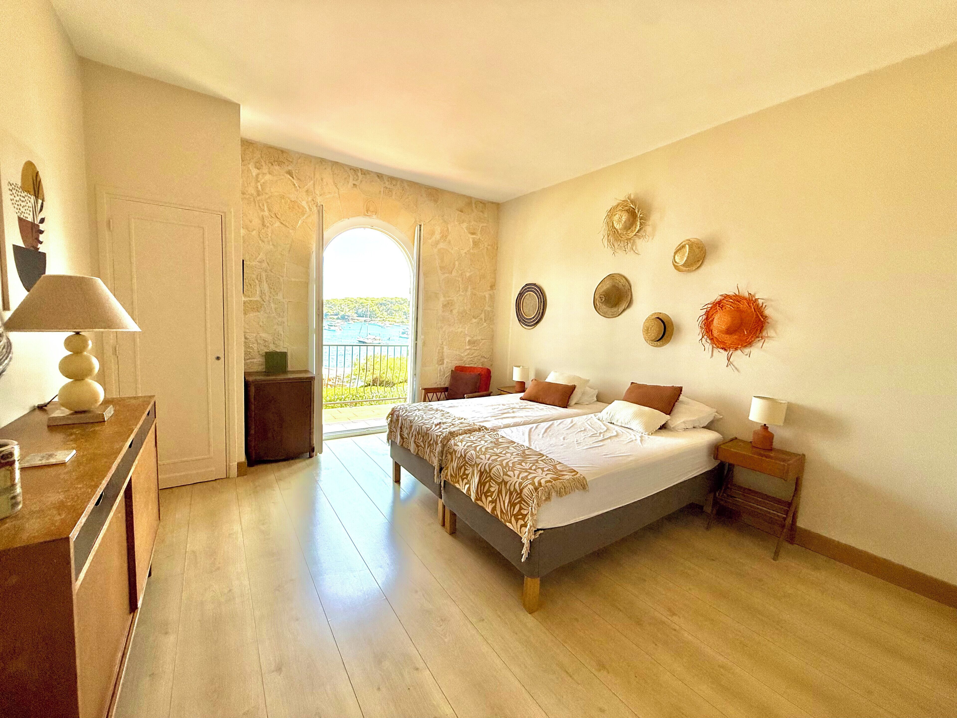 Ein Schlafzimmer mit einem Bett, Nachttischen, einem Schminktisch und Blick durch eine offene Tür.