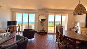 A spacious living area with a television, seating, a dining table, and a view of the sea through large windows. - Cap d'Antibes, view of La Garoupe beach – Sleeps 8 – Garden and terrace (Antibes)